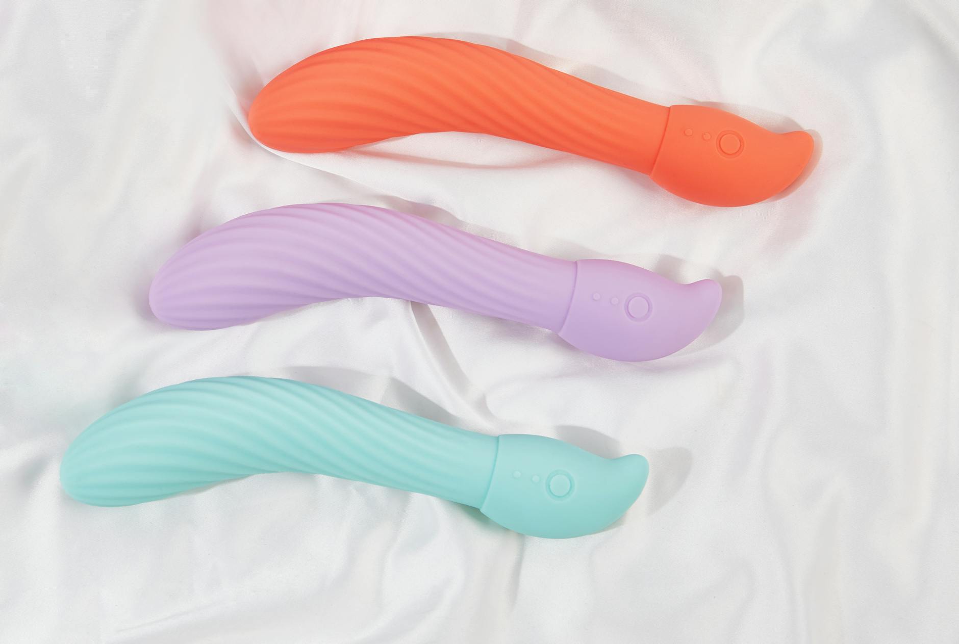 Tres vibradores de colores vibrantes sobre tela de algodón blanco, mostrando diferentes opciones de estimulación.