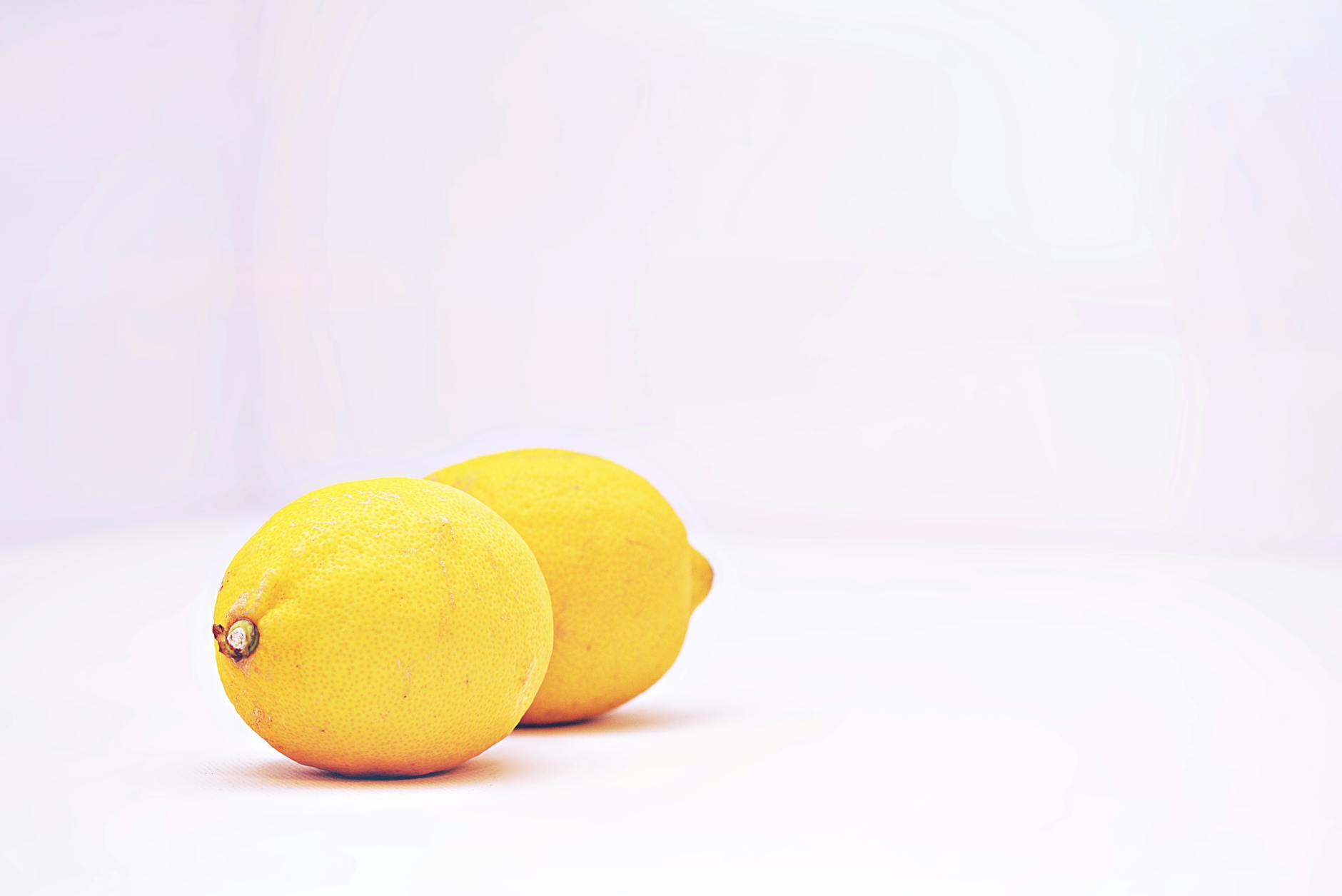 Dos limones vibrantes colocados contra un fondo blanco minimalista, mostrando frescura y simplicidad