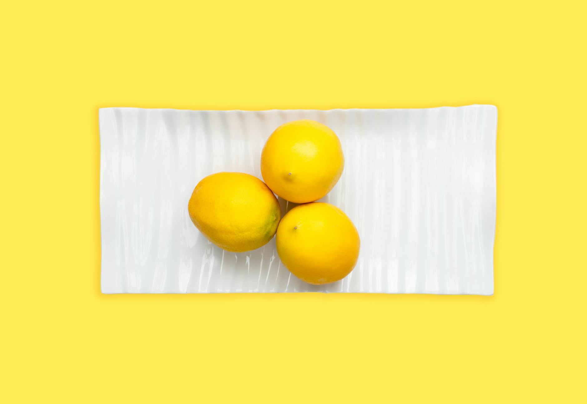 Limones frescos en plato blanco sobre fondo amarillo