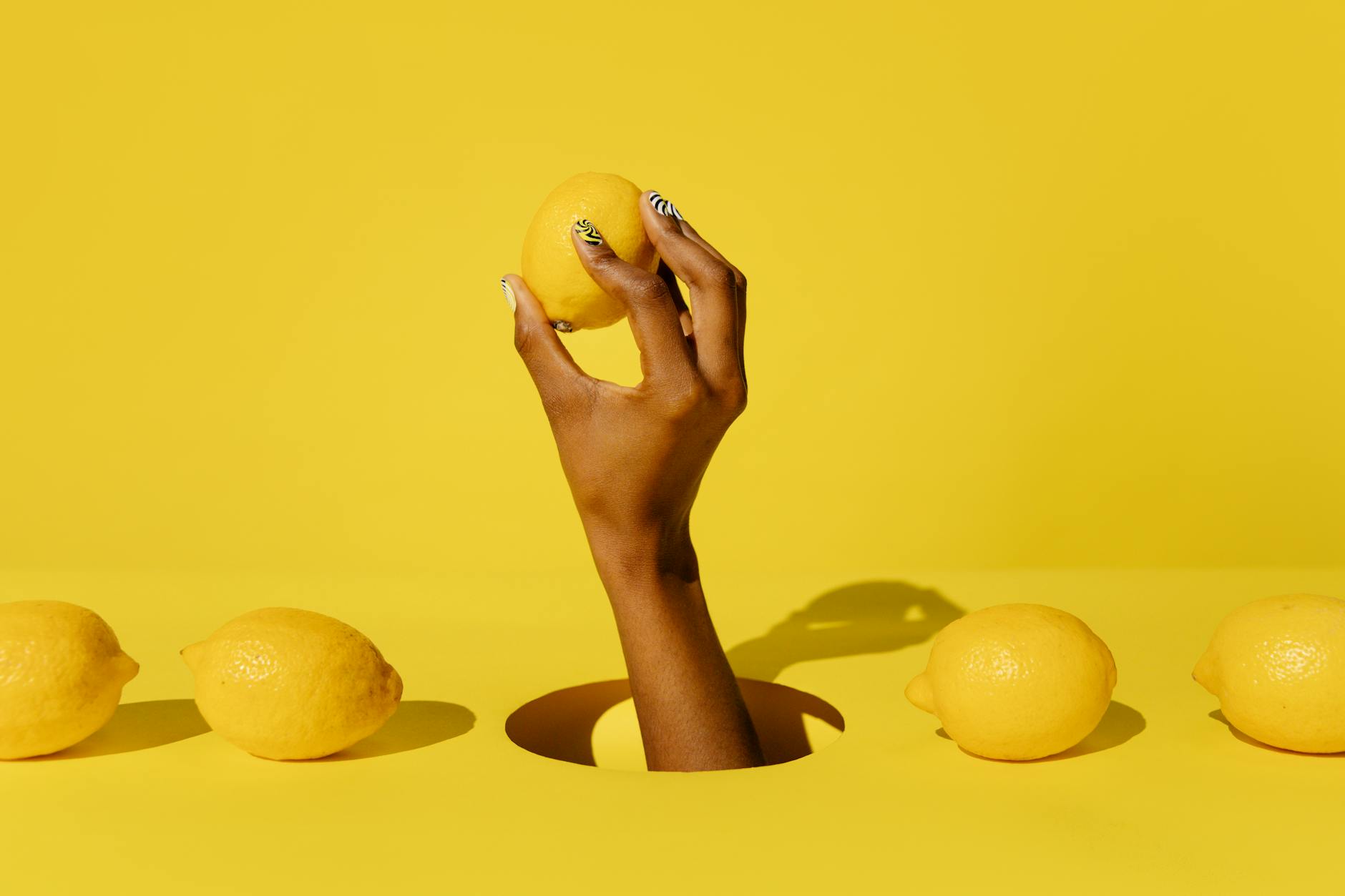 Una mano sostiene un limón fresco vibrante contra un fondo amarillo, transmitiendo una sensación cítrica y refrescante.