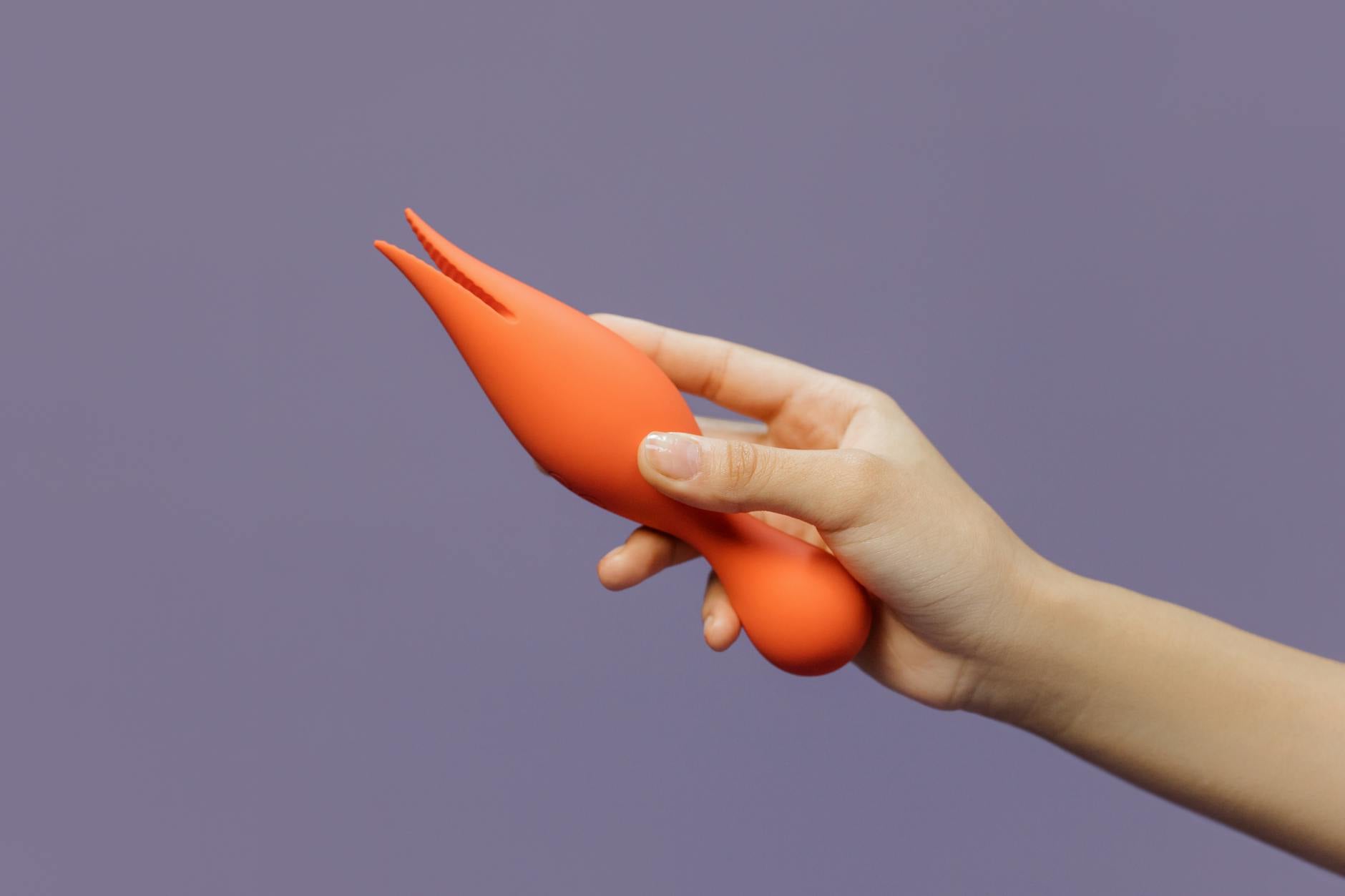 Mano sosteniéndose de un vibrador clitorídeo moderno contra un fondo minimalista, mostrando sensualidad contemporánea.