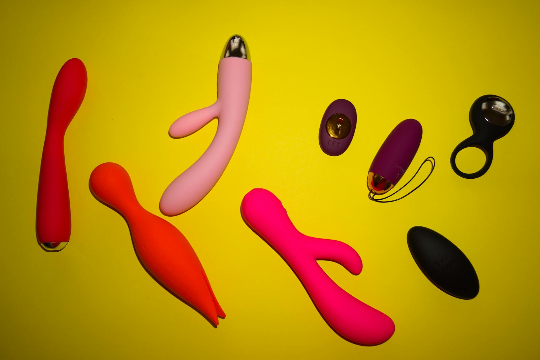 Vibradores de colores brillantes y diseños diversos organizados sobre fondo amarillo vibrante