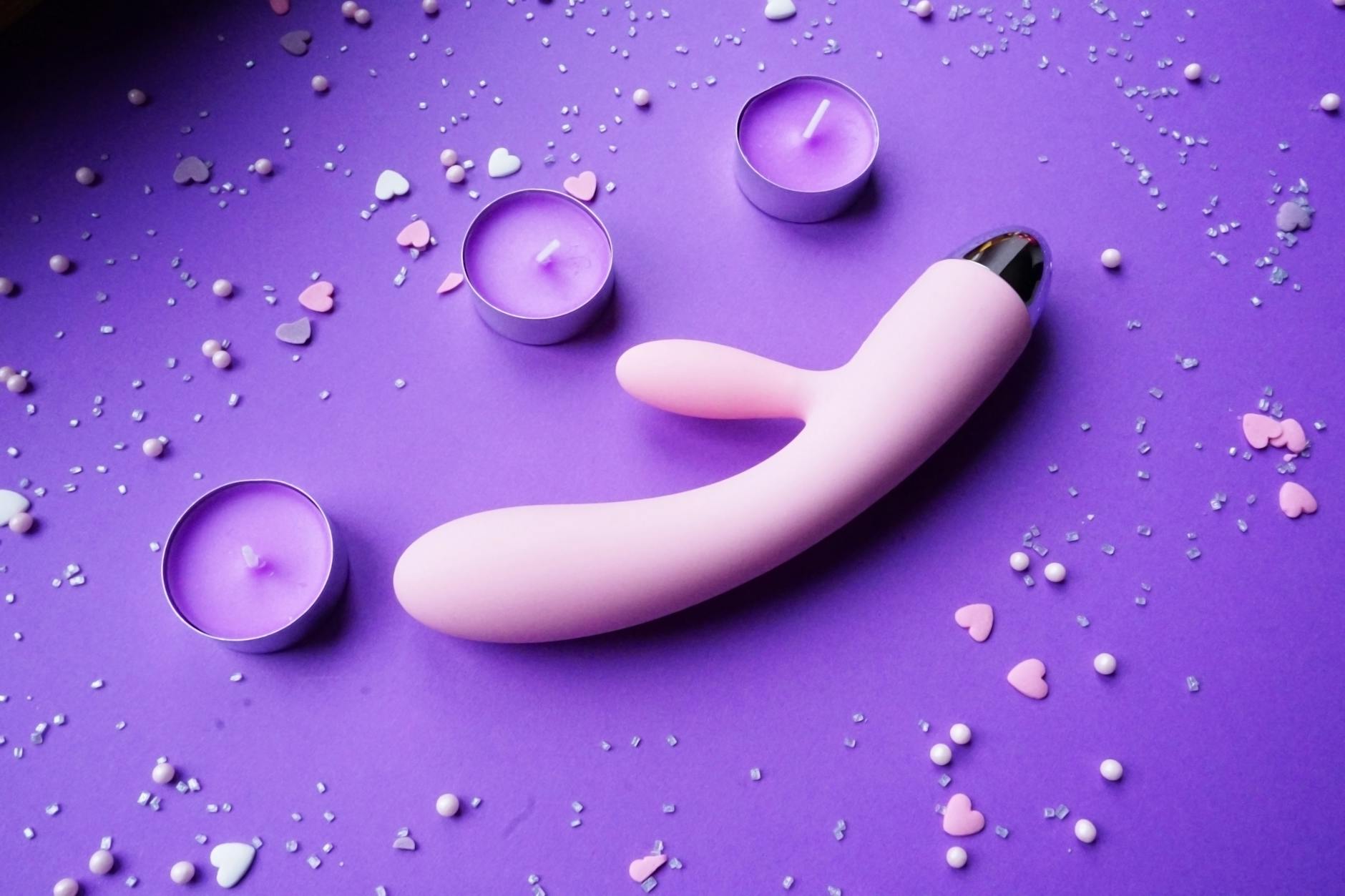 Vibrador de limón rosa sobre fondo púrpura con confeti en forma de corazón y velas para una atmósfera romántica